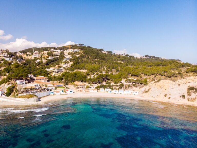 Catamarán fondeado en aguas cristalinas frente a los acantilados de Cala Blanca en Dénia