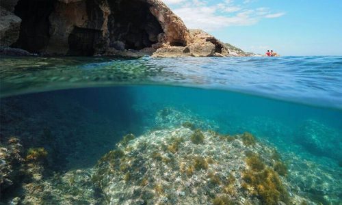 Catamarán aproximándose a la Cova Tallada al atardecer con los acantilados iluminados por el sol